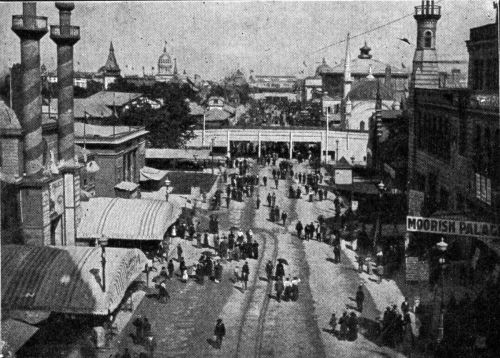 A historic street scene with people walking, tents, and buildings, showcasing a bustling market atmosphere.