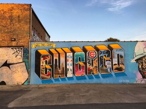 Colorful mural reading "Greetings from Chicago" with various images representing the city. Bright blue sky in the background.