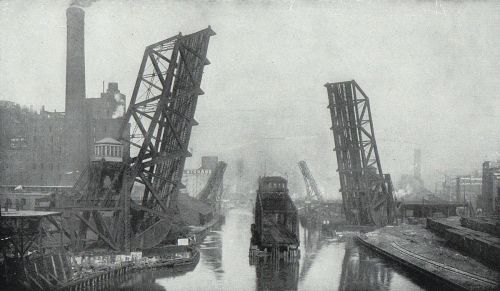 Black and white image of a canal with raised drawbridges and industrial buildings in the background, creating a foggy atmosphere.