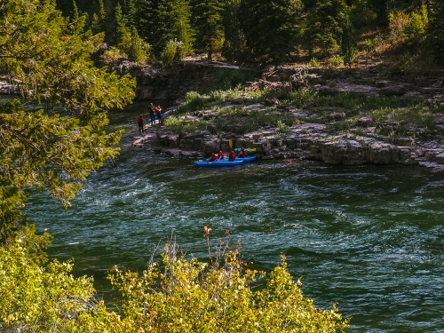 A group of kayakers paddles on a river surrounded by lush greenery and rocky banks.