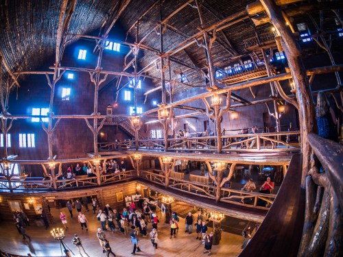 A spacious wooden hall with high ceilings, featuring rustic decor and people mingling on multiple levels.