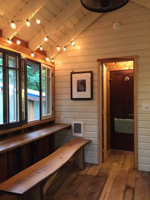 Cozy interior of a small room with wooden walls, string lights, a bench, and a door leading to a bathroom.