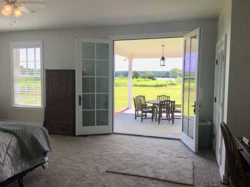 A spacious bedroom with a view of a patio and green landscape through open glass doors.