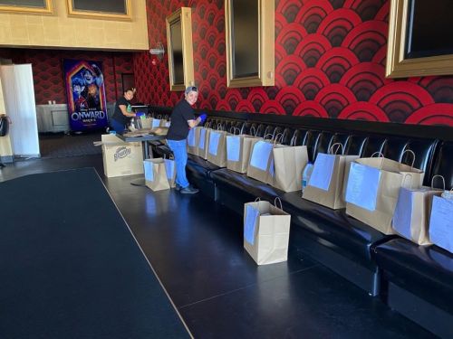 A person organizes paper bags on a black bench in a theater, with a colorful movie poster in the background.