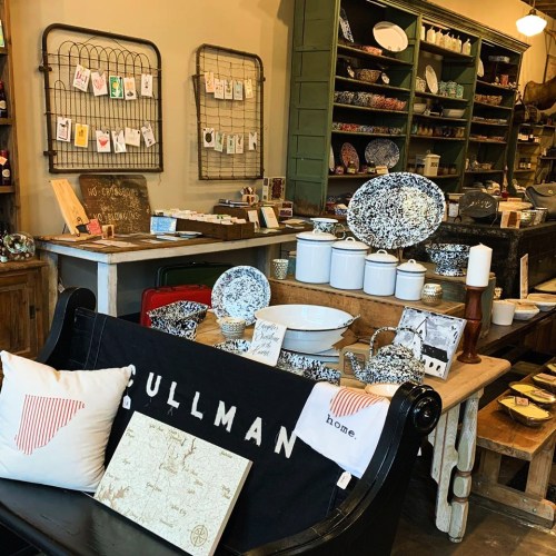 A cozy shop interior featuring vintage decor, dishware, and home goods displayed on wooden tables and shelves.