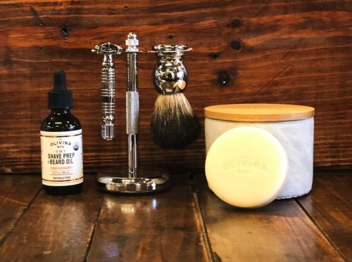 A shaving kit featuring a razor, brush, beard oil, and a cream container on a wooden surface.