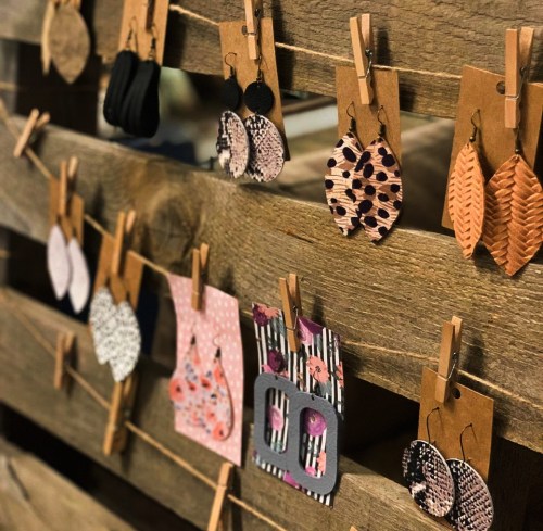 A display of various earrings hanging on a wooden board, featuring different shapes and patterns.