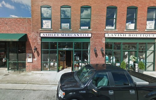 A brick building with two storefronts: "Ashley Mercantile" and "Lavish Boutique," with a parked black truck in front.