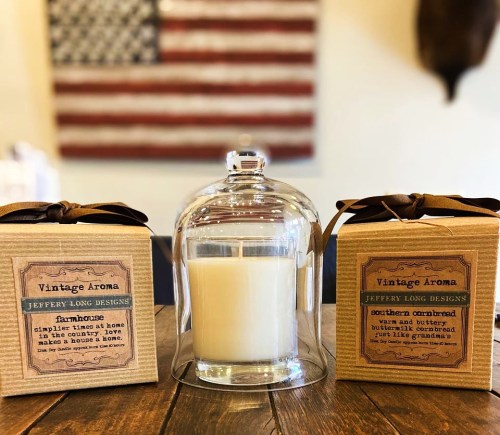 Two candle boxes labeled "Vintage Aroma" with a lit candle under a glass cloche, set against a rustic background.