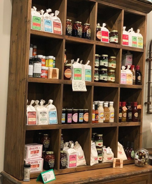 A wooden shelf displaying various jars, bottles, and bags of food products, organized in a grid pattern.