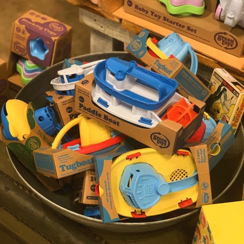 A metal bowl filled with colorful plastic toy boats and packaging, including paddle boats and tugboats.
