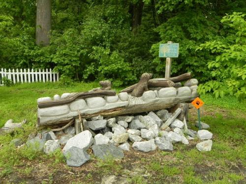 A stone and wood structure surrounded by rocks, with a sign and greenery in the background.