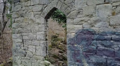 A stone archway in a dilapidated structure, surrounded by trees and overgrown vegetation.