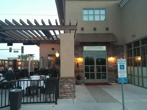 Exterior view of a restaurant with a patio, featuring a stone facade and outdoor seating. Reserved parking sign visible.