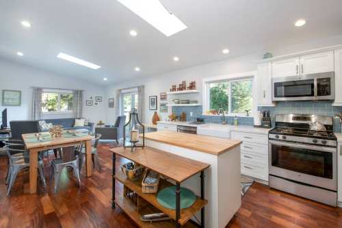 Bright, modern kitchen with white cabinets, stainless steel appliances, and a wooden dining table in an open layout.