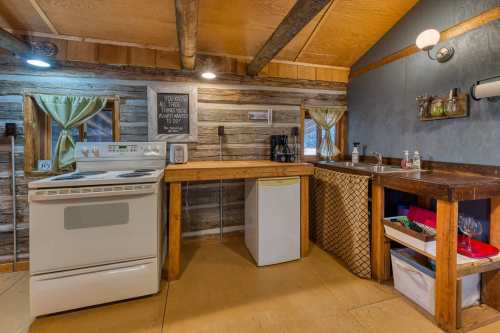 Cozy kitchen with wooden beams, stove, sink, and rustic decor, featuring a small fridge and coffee maker.