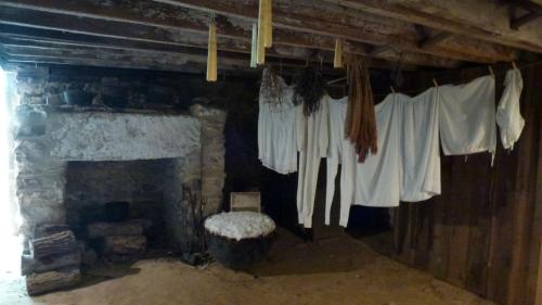 Interior of a rustic room with a stone fireplace, hanging white garments, and dried herbs on a clothesline.