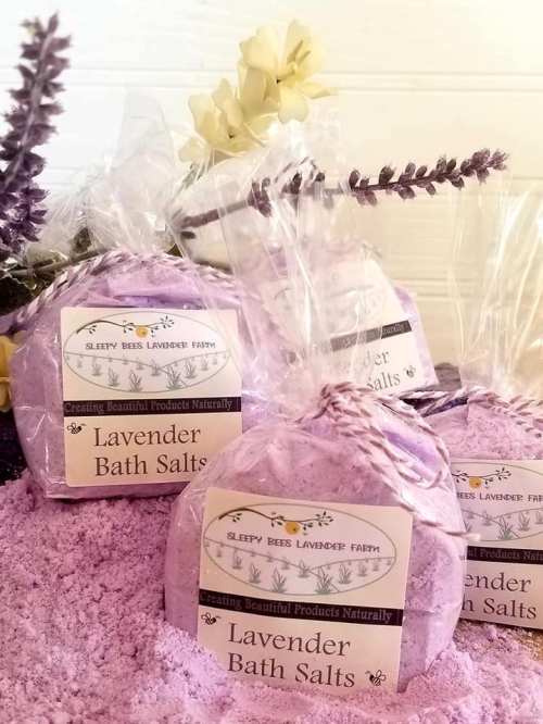 Bags of lavender bath salts with purple crystals, surrounded by lavender sprigs and a flower.