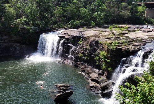 A scenic waterfall cascades into a serene pool, surrounded by lush greenery and rocky formations.