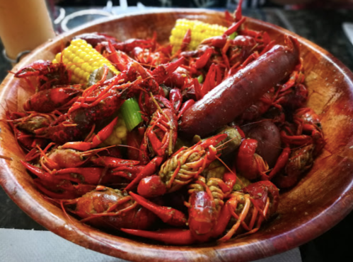 A wooden bowl filled with crawfish, corn, and sausage, showcasing a vibrant seafood feast.