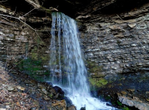 A serene waterfall cascading over rocky cliffs, surrounded by moss and natural greenery.