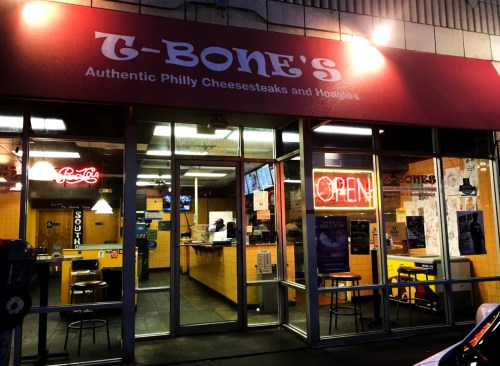 Exterior of T-Bone's, a restaurant featuring a red awning, open sign, and large windows showcasing the interior.