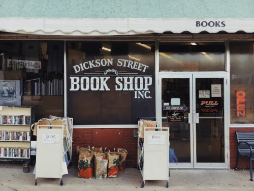 Exterior of Dickson Street Book Shop, featuring a sign, open door, and book carts outside.