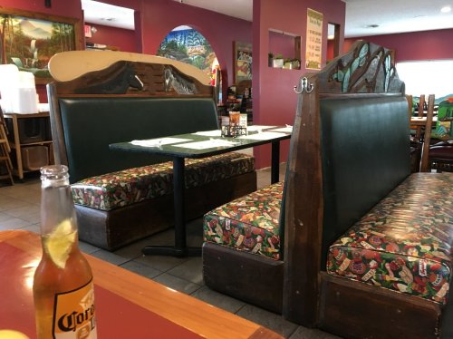 Cozy restaurant interior featuring colorful booths and a table, with a bottle of beer in the foreground.