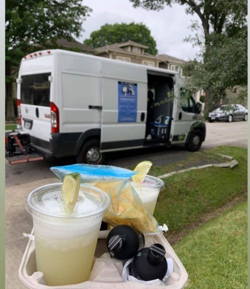 A tray of drinks and snacks in front of a food truck parked on a street, with trees and cars in the background.