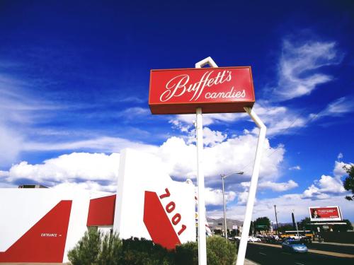 Sign for Buffett's Candies against a blue sky with clouds, featuring a modern building and a clear street view.