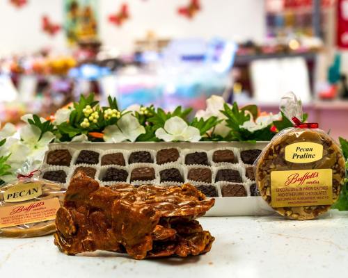 A display of assorted chocolates, pecan praline, and a bag of pecan candies, surrounded by decorative flowers.