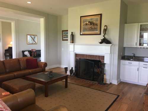 Cozy living room with a brown leather sofa, coffee table, fireplace, and a wall-mounted artwork. Light and inviting atmosphere.