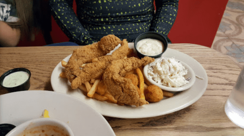 A plate with fried chicken, fries, coleslaw, and dipping sauce on a wooden table.