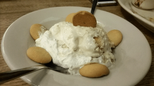 A bowl of whipped cream topped with a cookie, surrounded by vanilla wafers and a spoon.