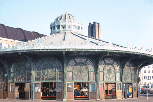 Historic carousel pavilion with ornate architecture and large windows, showcasing a colorful carousel inside.