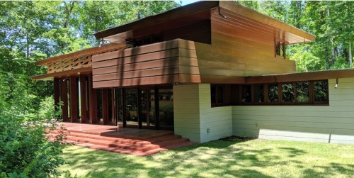 A modern two-story house with a wooden exterior, large windows, and a landscaped yard surrounded by trees.
