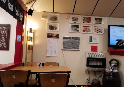 Interior of a small restaurant featuring a table, wall decor with food images, a calendar, and an air conditioning unit.