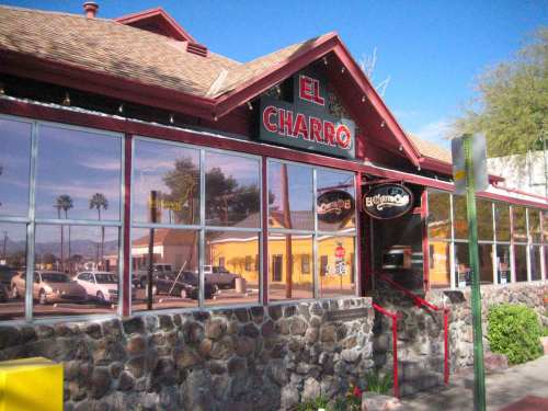 Exterior of El Charro restaurant with a stone facade, large windows, and a red roof under a clear blue sky.