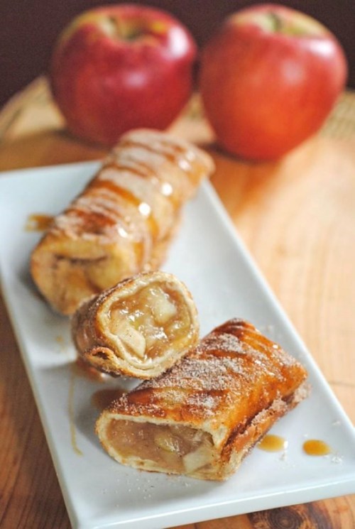 A plate of apple strudel slices drizzled with caramel, with whole apples in the background.