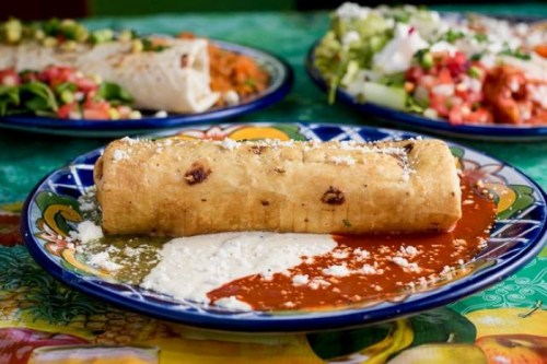 A crispy rolled tortilla filled with ingredients, served on a colorful plate with red and white sauces.