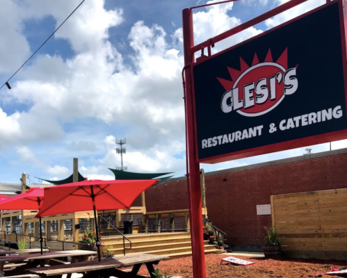 Sign for Clesi's Restaurant & Catering with red umbrellas and outdoor seating in a sunny setting.