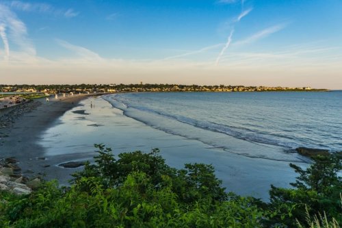 A serene beach scene at sunset, with gentle waves lapping the shore and a distant shoreline under a clear blue sky.