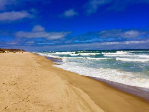 A sandy beach with gentle waves under a blue sky with scattered clouds.