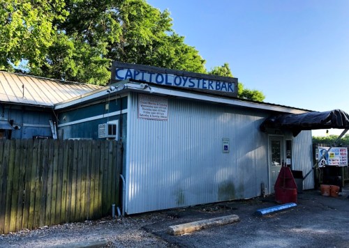 Exterior of Cap't Lou's Oyster Bar, featuring a blue and white building with a sign and a wooden fence.