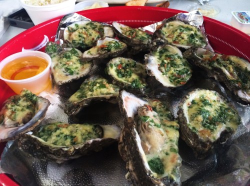 A platter of baked oysters topped with a green herb mixture, served with a small cup of sauce.
