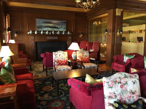 Cozy lounge with floral armchairs, a fireplace, and warm lighting, featuring wooden accents and a colorful rug.
