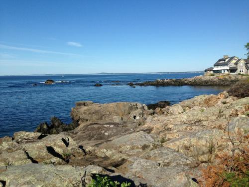 A rocky shoreline with calm blue waters and a house overlooking the ocean under a clear blue sky.