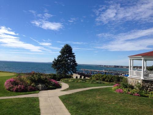 A scenic view of a waterfront with a gazebo, lush green grass, colorful flowers, and a clear blue sky.