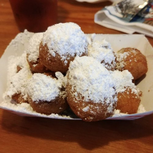 A plate of golden-brown dough balls dusted with powdered sugar, served in a casual dining setting.
