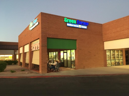 Exterior of Green Corner restaurant with outdoor seating, brick facade, and illuminated signage at dusk.
